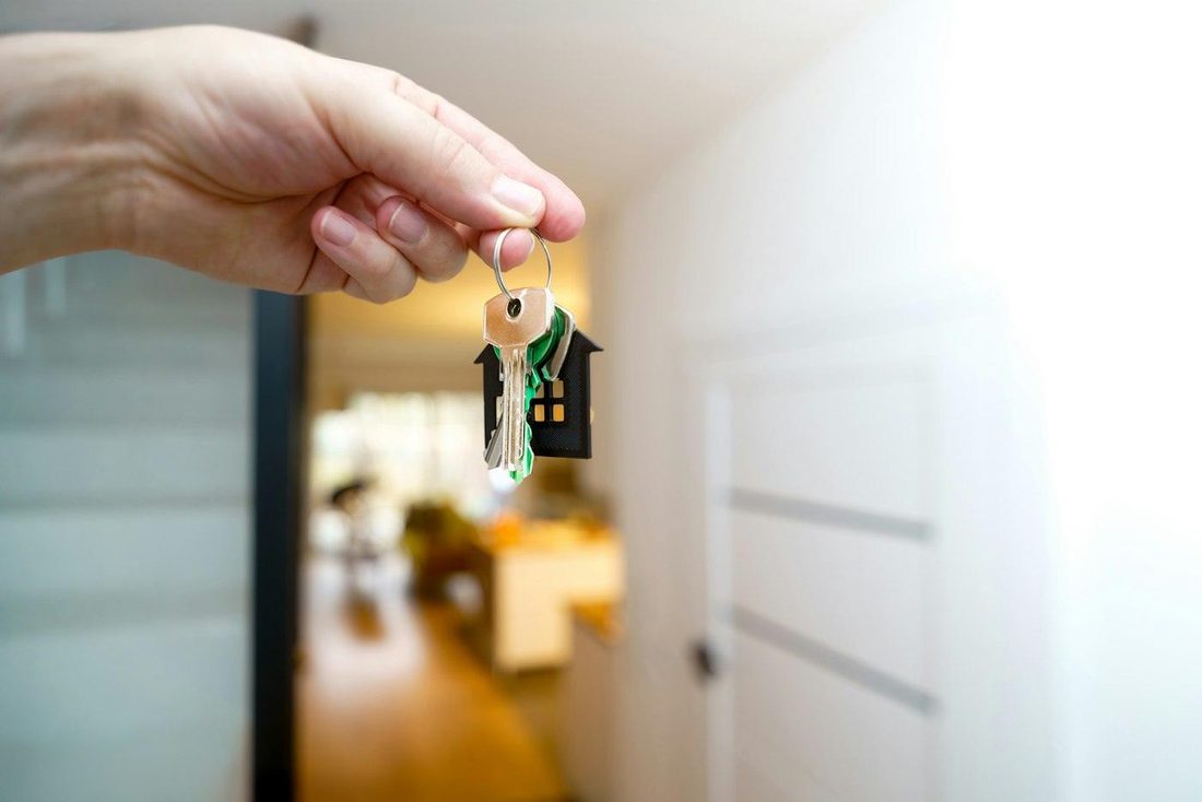 Une main tend un trousseau de clés à porte-clés en forme de maison, dans l'entrée d'un logement