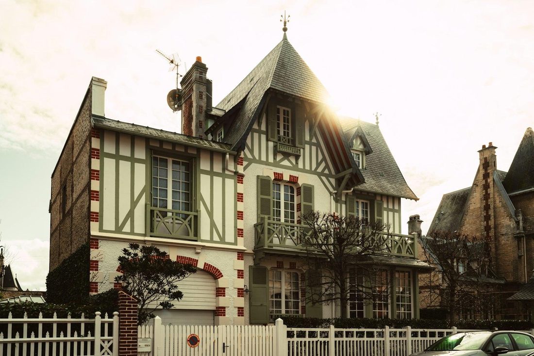 Maison ancienne à colombages, toiture en ardoise et volets verts, vue depuis la rue