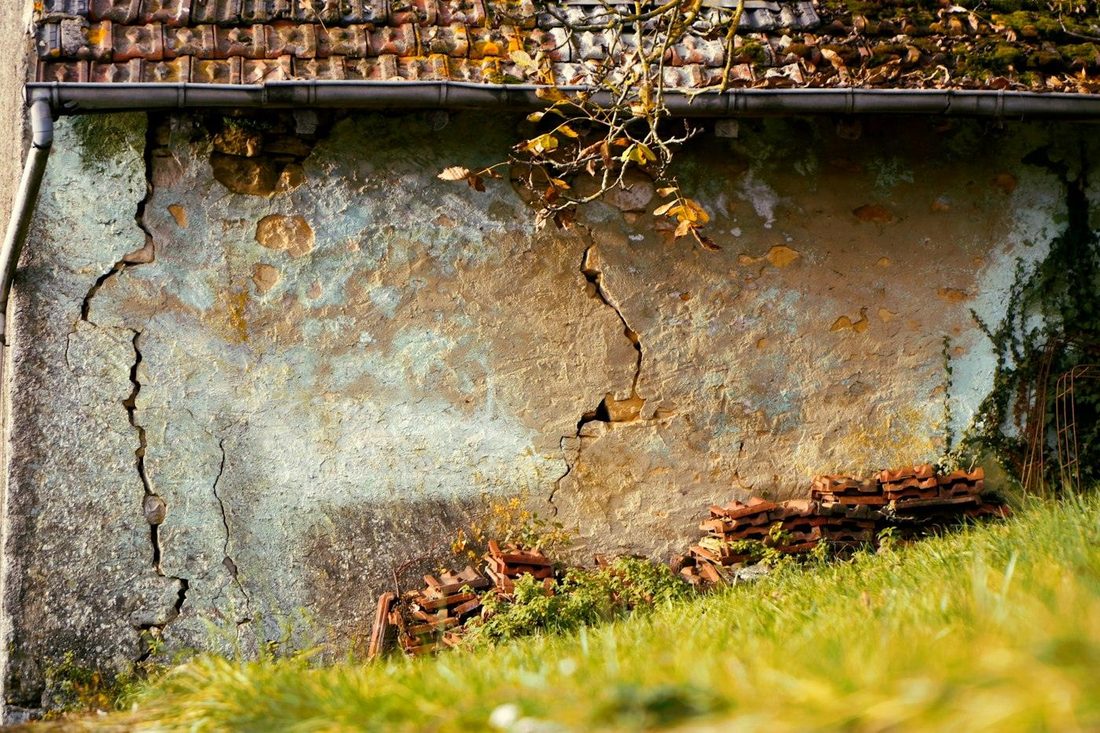 Mur ancien dont l'enduit se décolle, parcouru de deux fissures verticales, sous une couverture en tuiles
